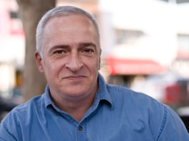 Man with grey hair and a blue shirt grins