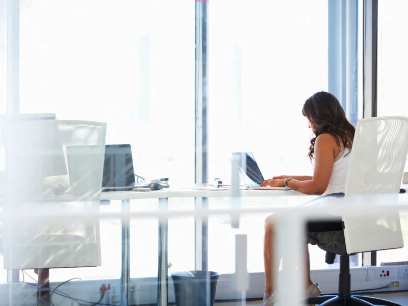 woman sits at a desk on her laptop in a business office