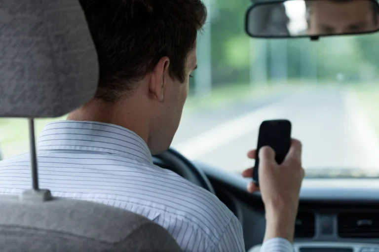 Man looks at and interacts with his cell phone while behind the wheel of a car
