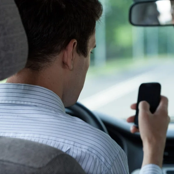 Man looks at and interacts with his cell phone while behind the wheel of a car