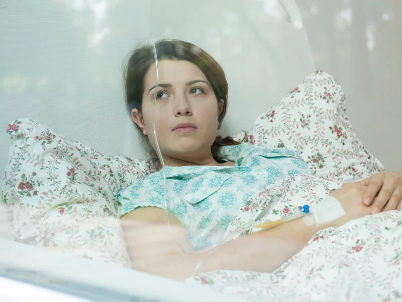 woman lies in hospital bed, arm hooked up to an IV drip