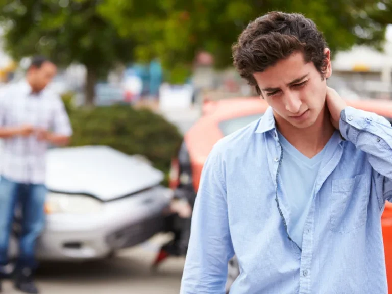 man walking away from a car accident holding the back of his neck and grimacing