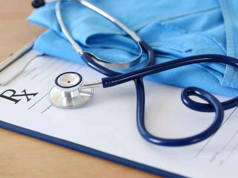 A stethoscope and a set of scrubs sitting on top of a prescription script