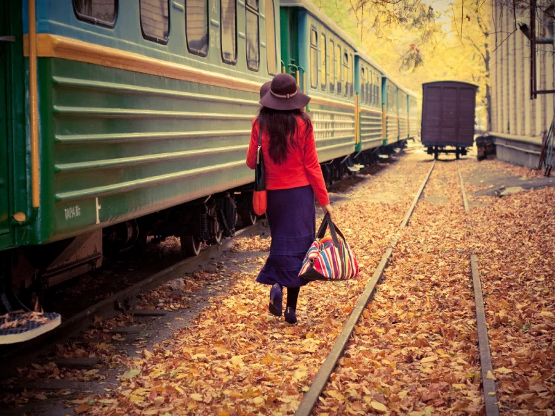 Lady walks along parked train, duffel bag in hand