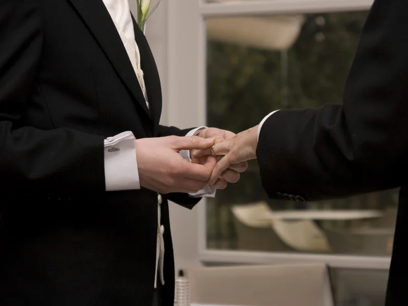 Two men exchange wedding rings in suits